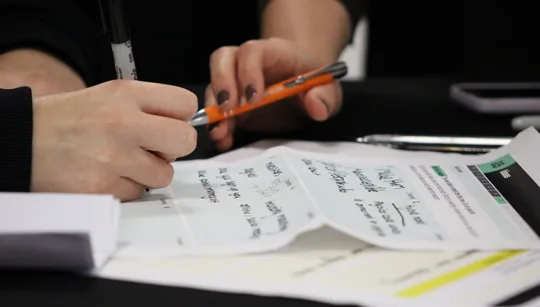 Close-up of a young person’s hands writing ideas on a team workbook sheet at Fresh Meet CIC’s Innovation Lab, Magna