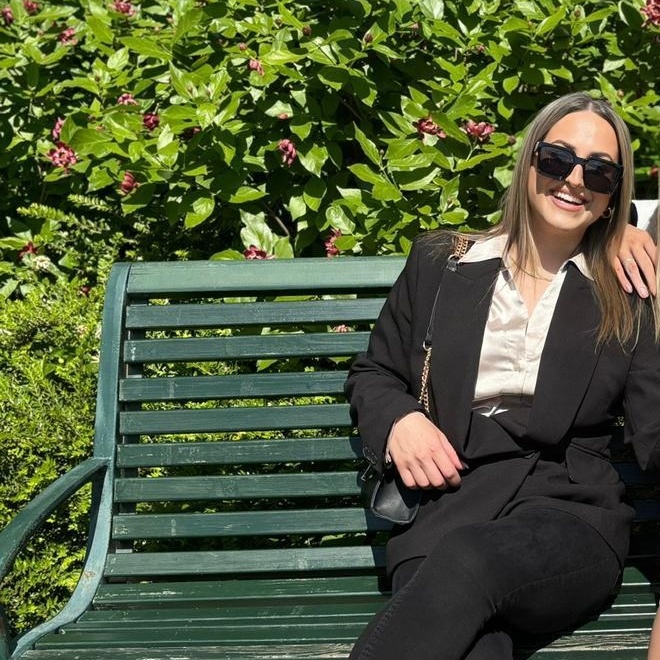 Sidra Rashid ler när hon sitter på en grön bänk omgiven av grönska