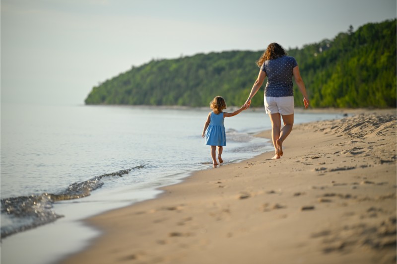 a mom and daughter holding hands walking along the beach