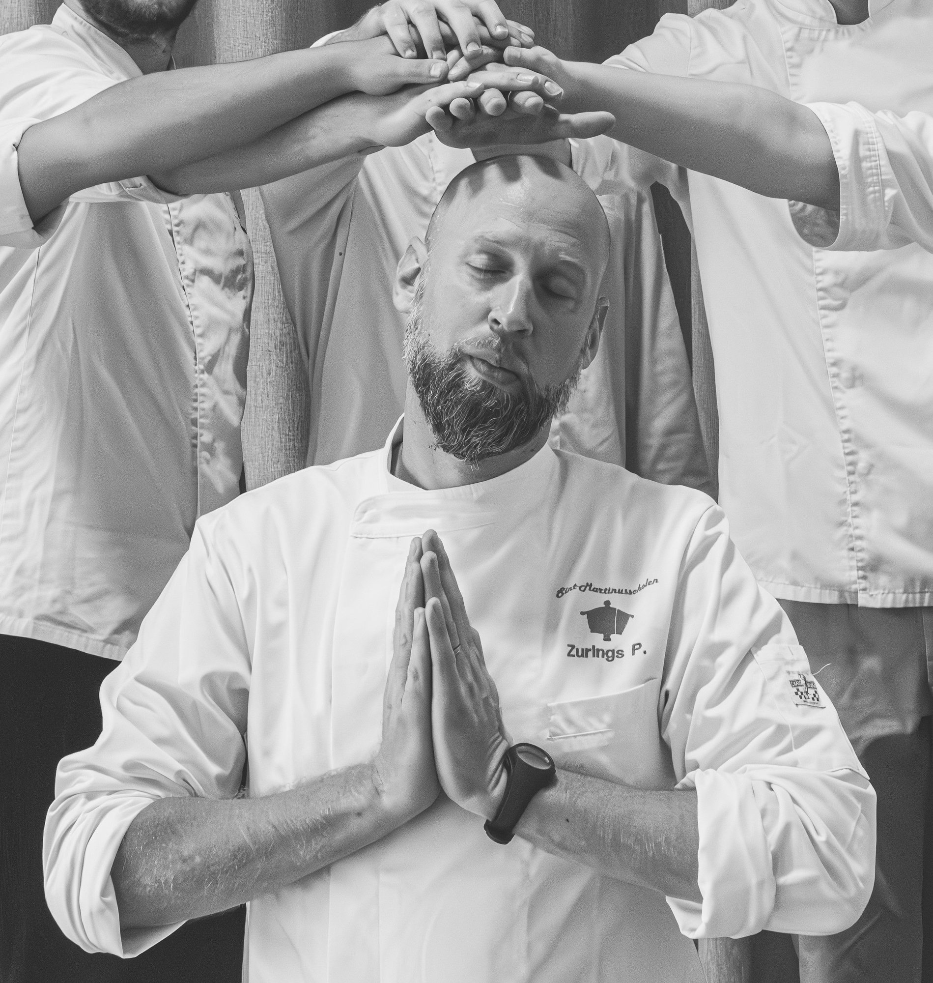 Photo en noir et blanc du chef Pieter Zurings en veste de cuisine blanche, entouré de ses élèves