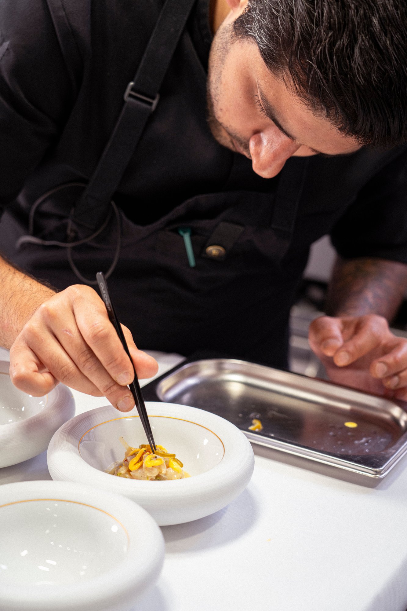 Photo couleur du chef Shayan Zaghian dressant une assiette à la pince