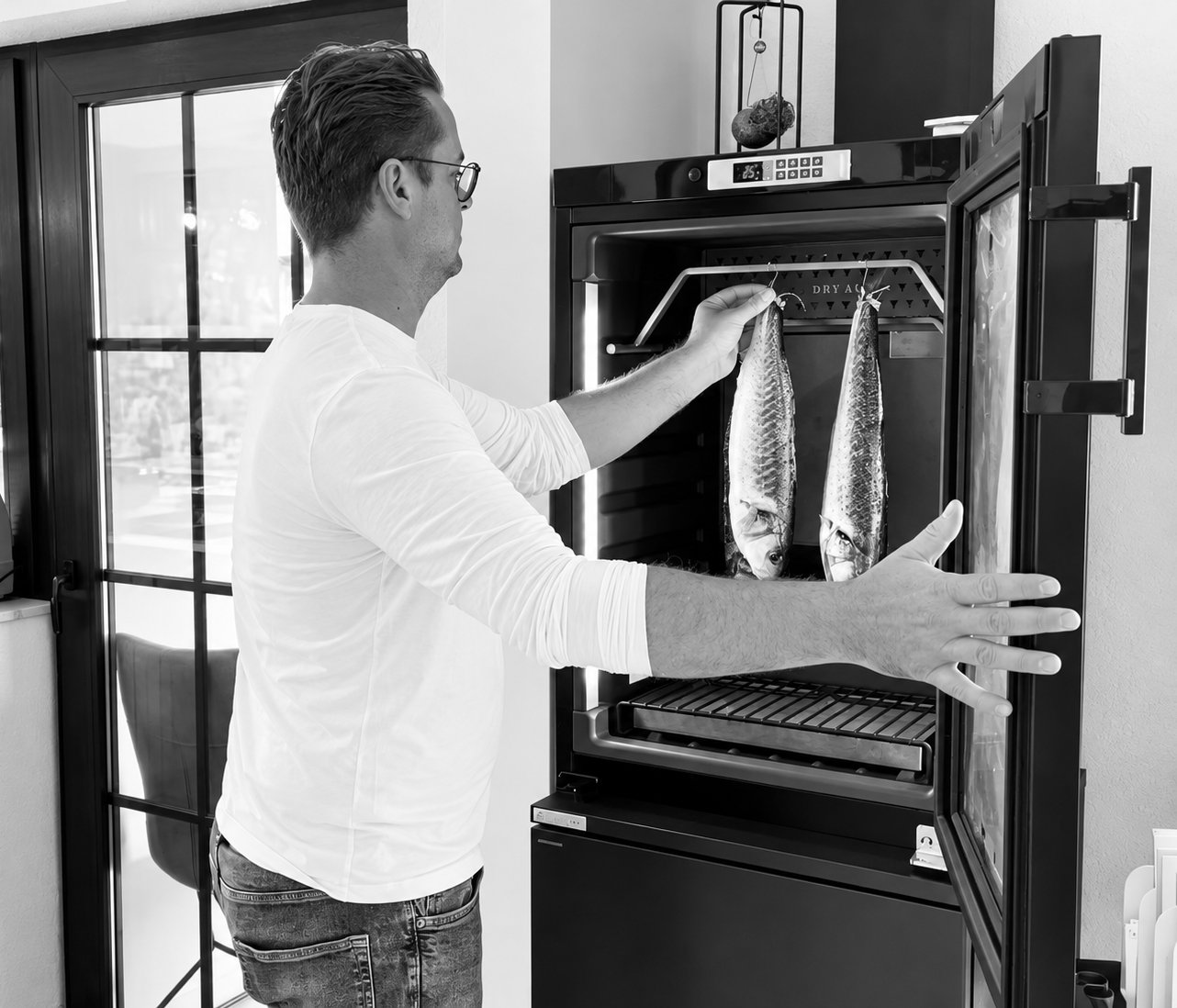 Photo en noir et blanc du chef Gregory Slembrouck suspendant du poisson dans une armoire de maturation