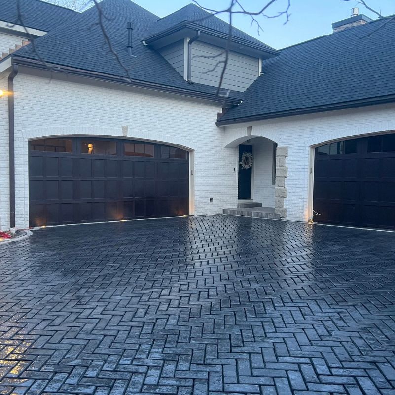 Modern house exterior with white brick walls, dark garage doors, and herringbone patterned driveway.