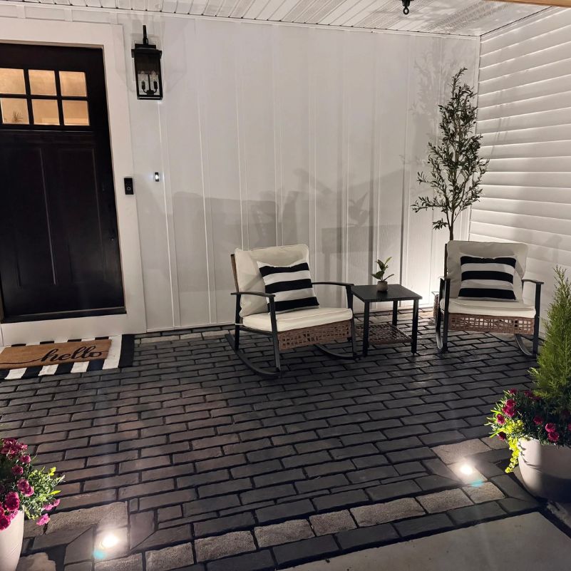 Cozy patio with two cushioned chairs, a small table, potted plants, and a “hello” doormat by a dark door.