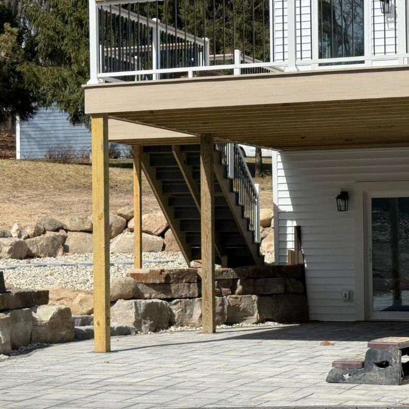 Backyard patio with stone retaining walls, concrete pavers, wooden deck, and staircase leading up.