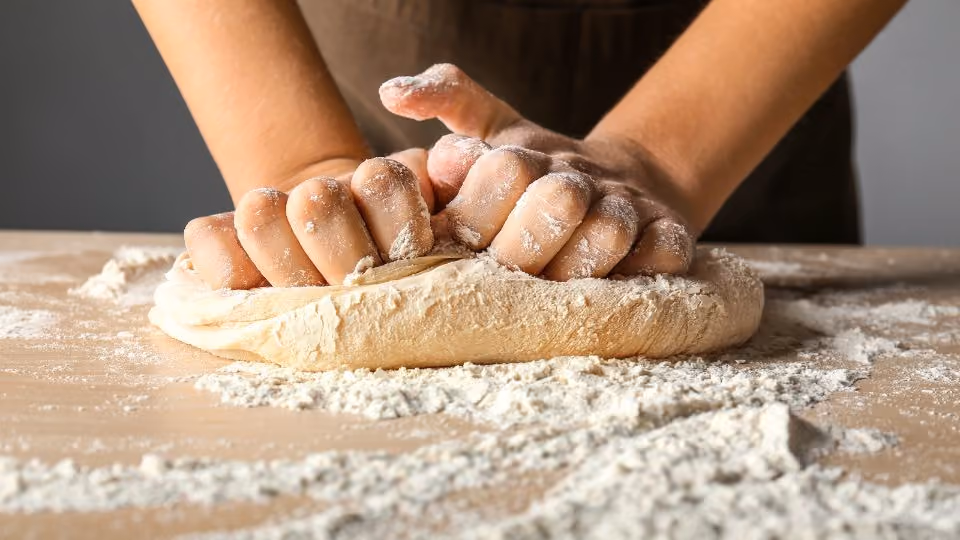 Hands kneading dough on a floured wooden surface.