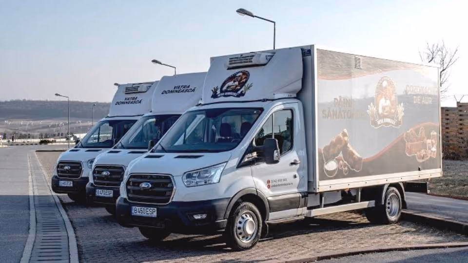 Three white delivery trucks with corporate branding parked side by side on a paved area under streetlights.
