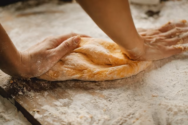 Hands kneading dough on a floured wooden surface.