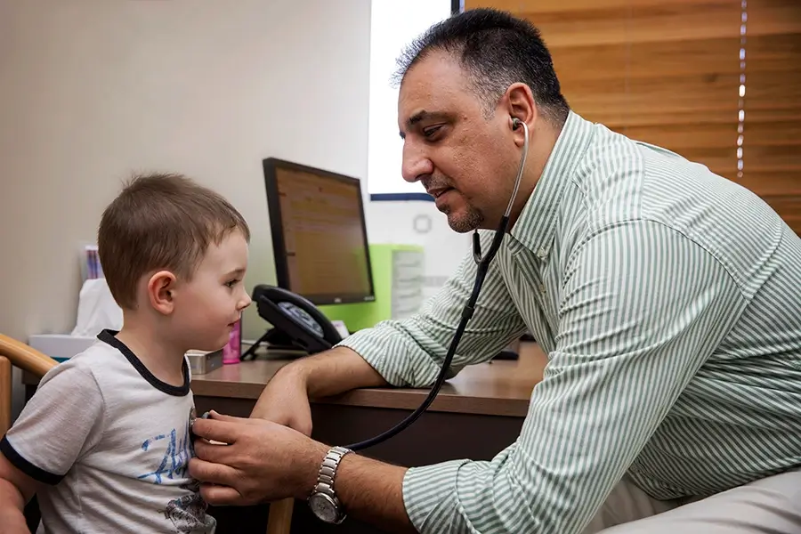 Doctor with stethoscope testing small child. Both are smiling.