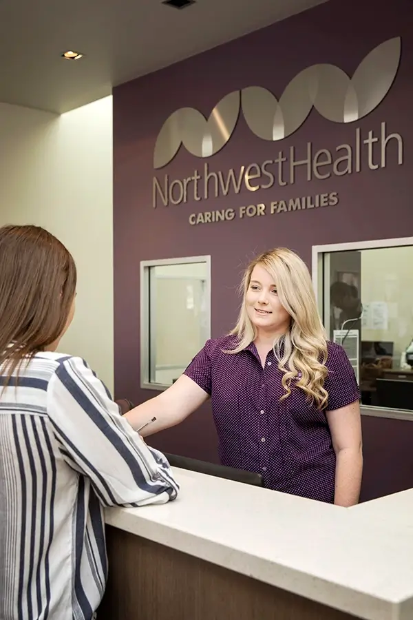 Receptionist at front counter speaking with customer. She is 