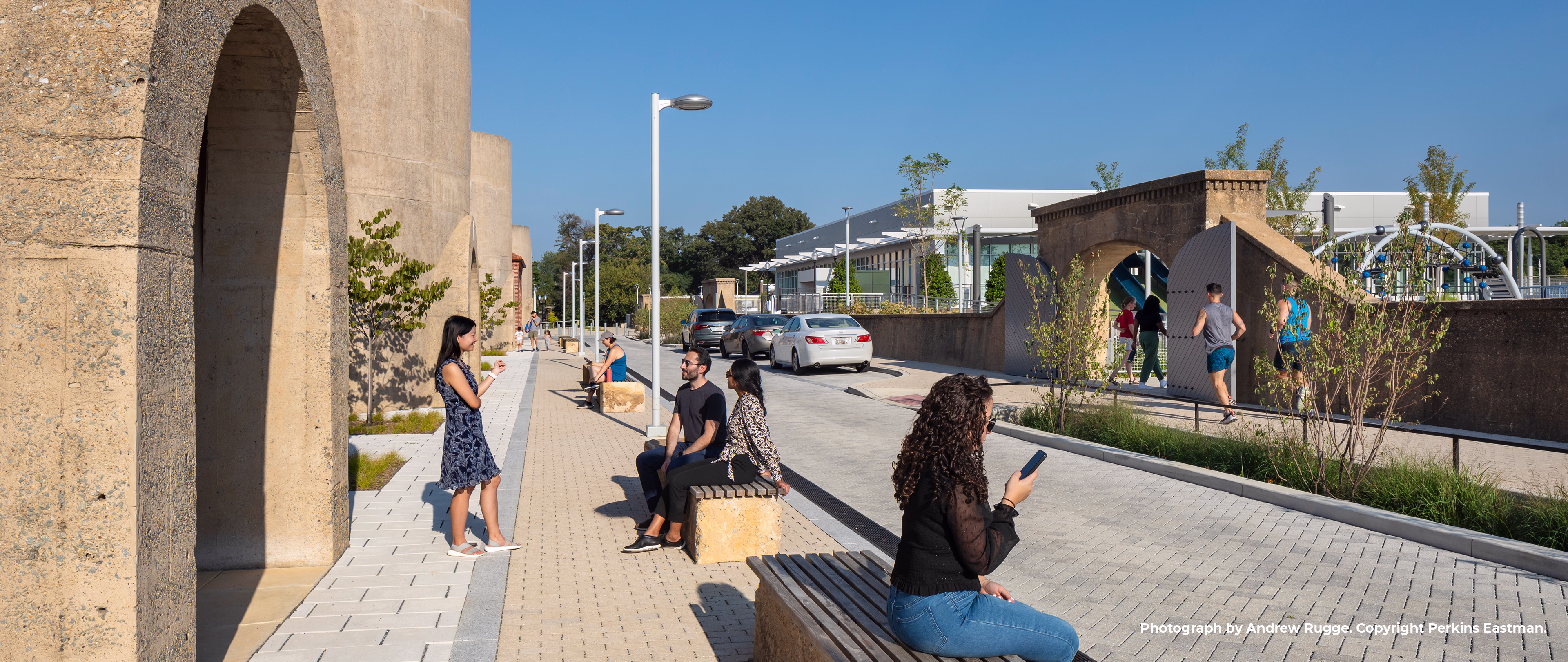 Visitors sit and chat on benches near the preserved silos while others run past.