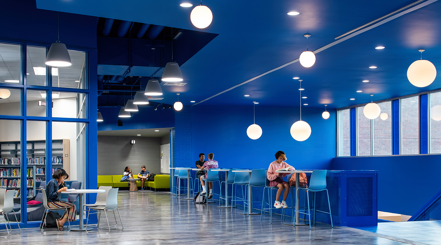 A photo of students sitting at high top tables near windows with abundant natural light.