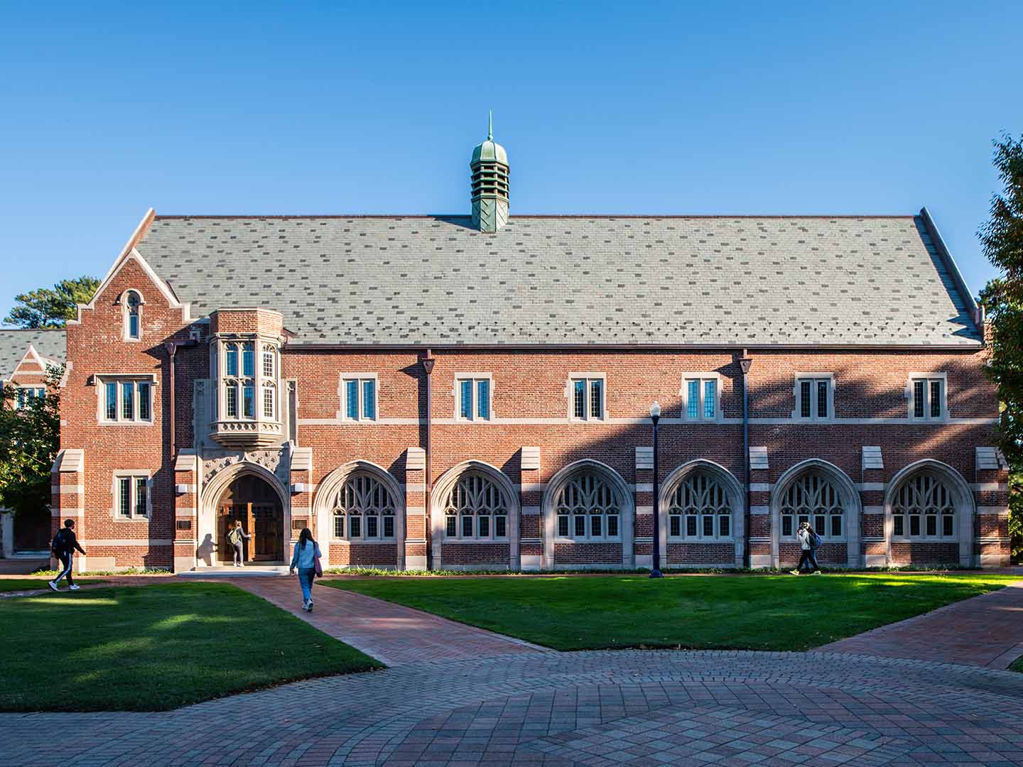 A photo of students walking towards a brick building on a college campus.