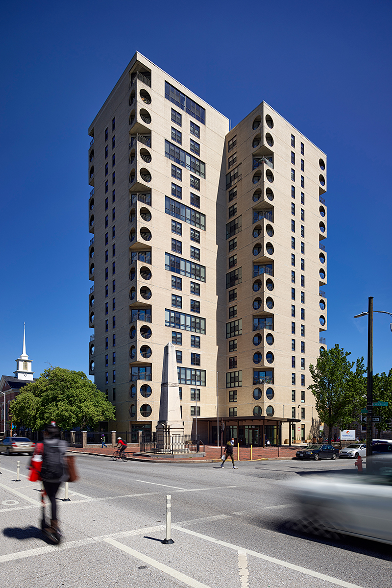 A photo of people outside an apartment building on a busy street corner.