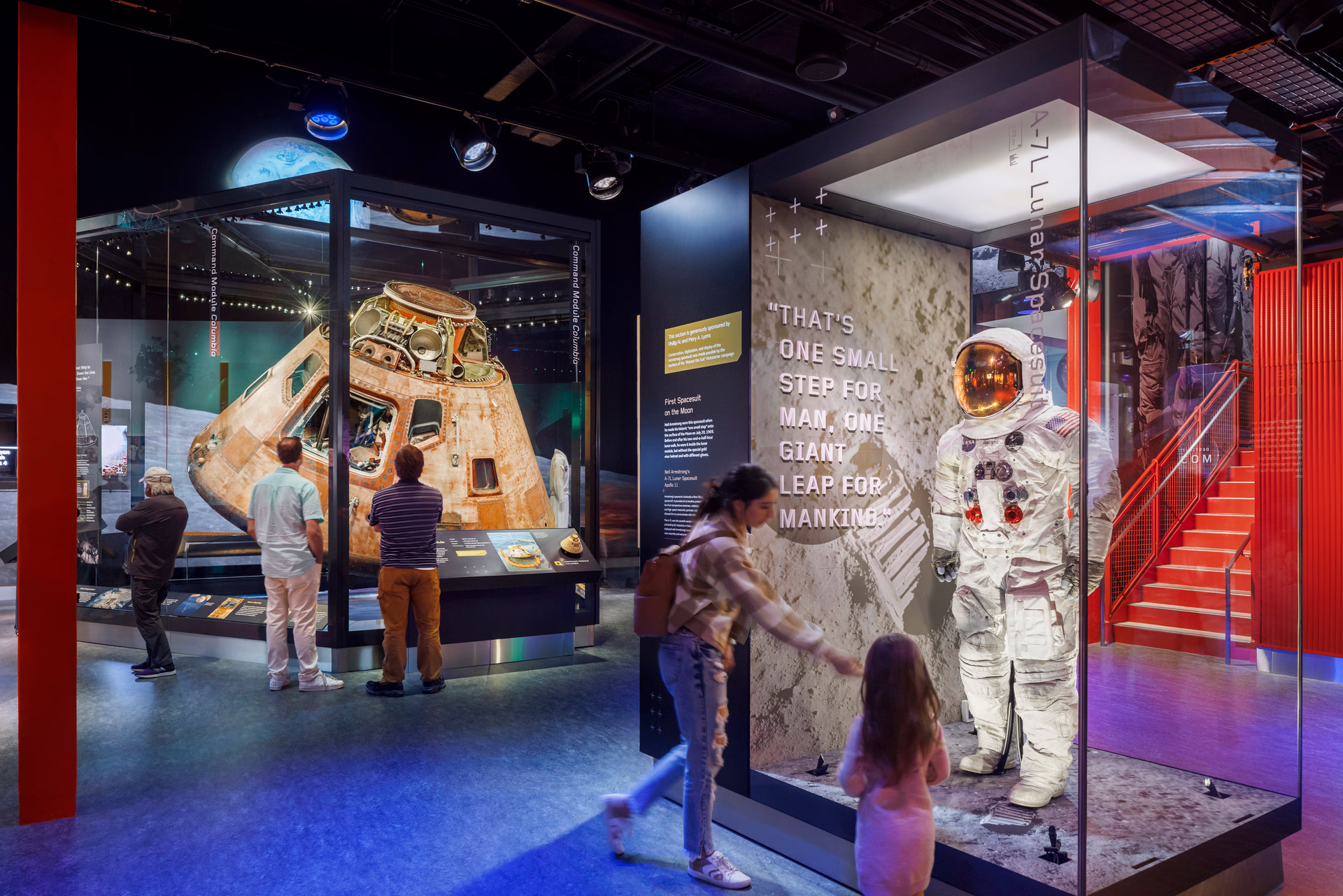 A photo of people looking at museum exhibit cases holding a space suit and spacecraft command module.