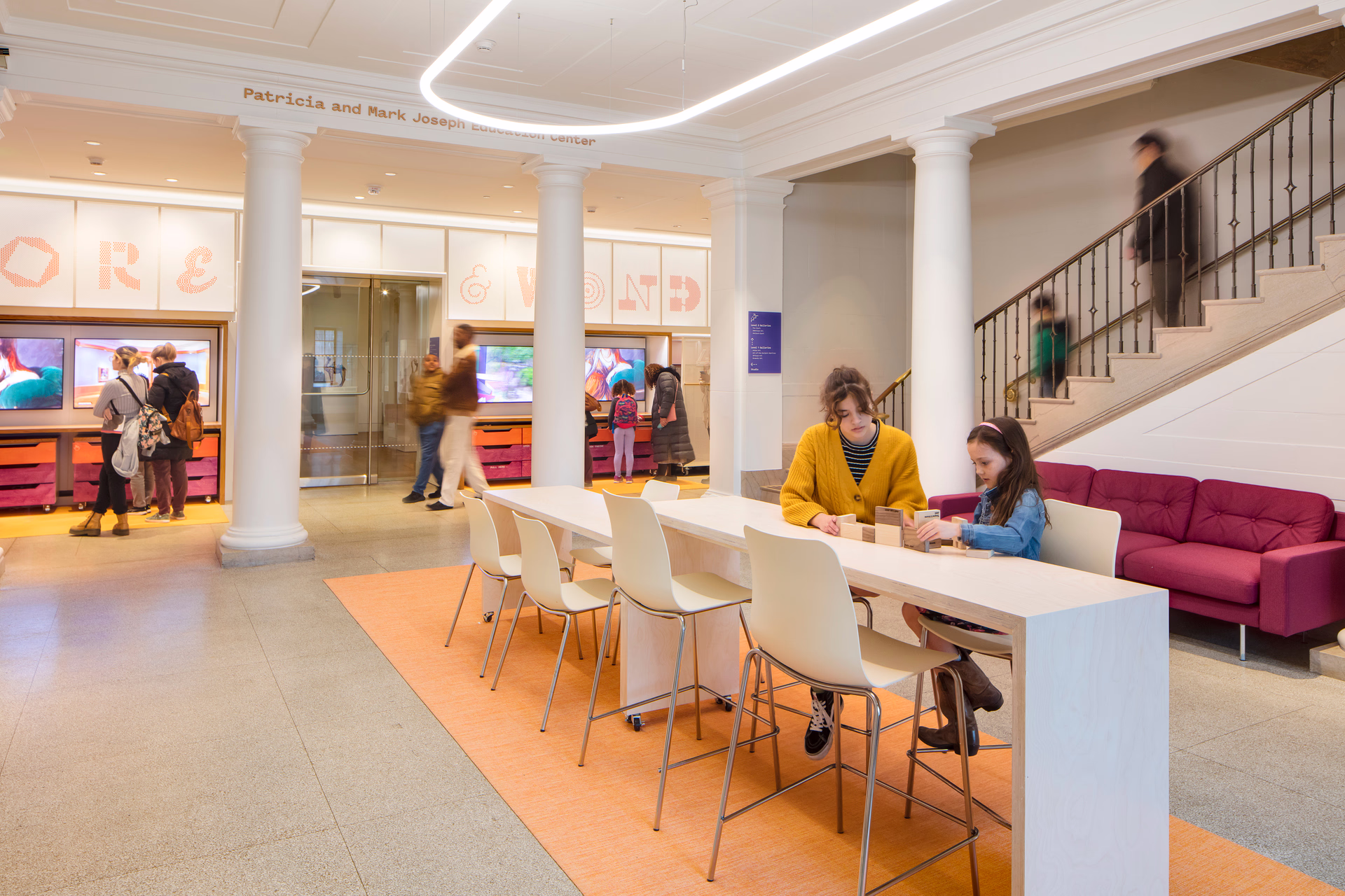An interior photo of a colorful space within a historic museum building. Families play with blocks and look at digital screens.