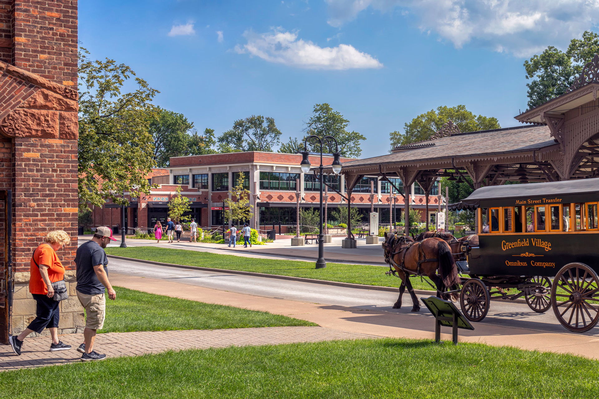 An exterior photo of a living history museum with historic buildings, a horse-drawn carriage, and visitors walking around.