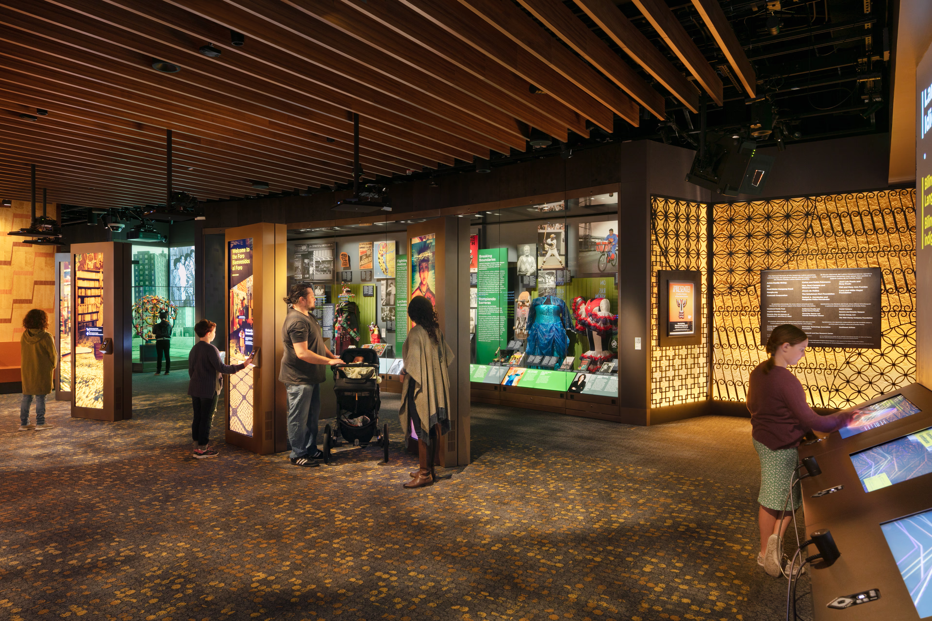 An interior photo of an exhibit gallery with people looking at interpretive text and colorful artifacts in vitrines.