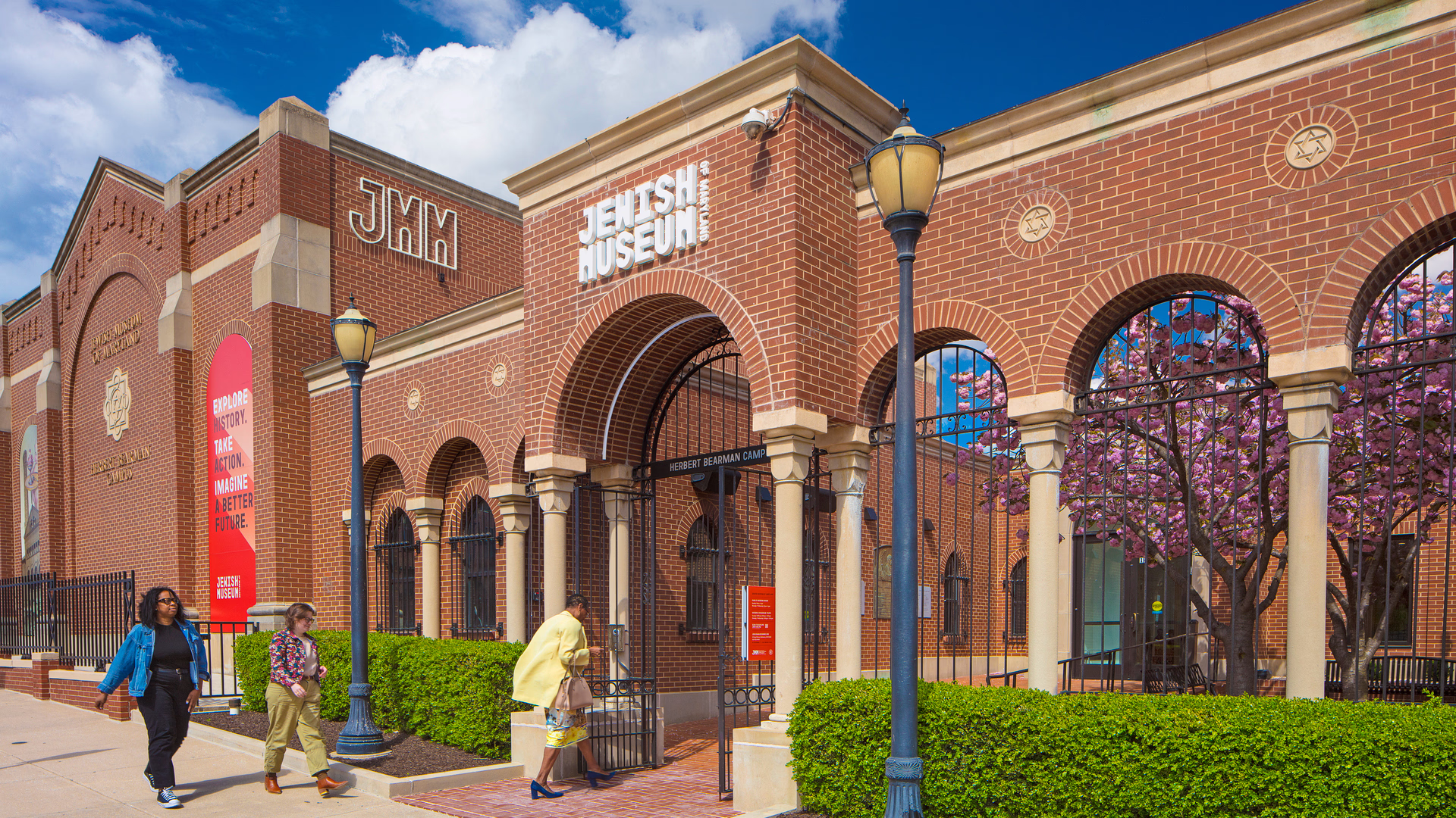 An exterior photo of a museum with people walking through the front gates and into a courtyard.