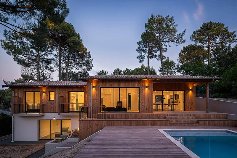 Villa bois avec piscine et terrasse au crépuscule, entourée de pins