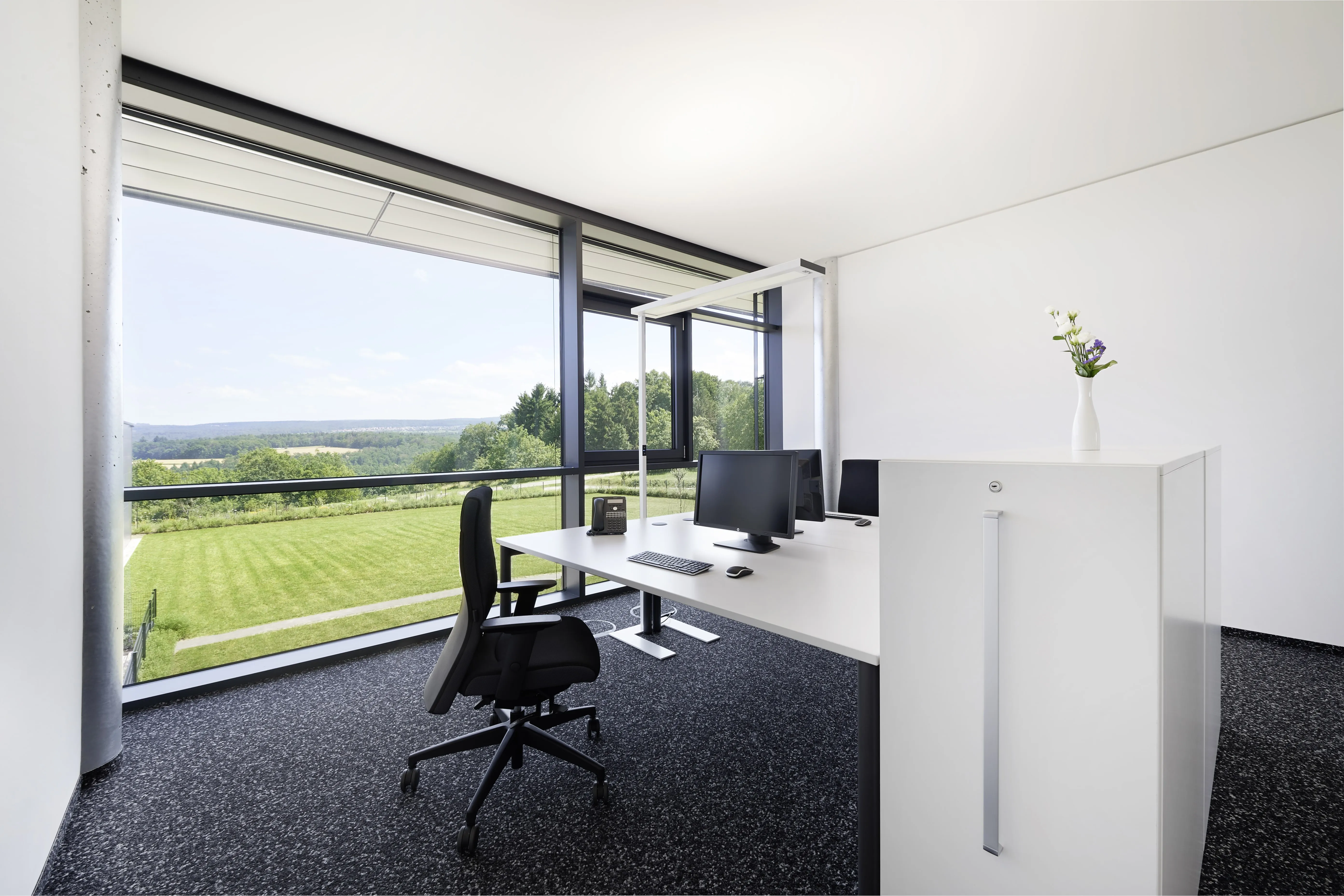 Ergonomischer Schreibtisch und Bürostuhl in einem Büro von Kohnle & Partner, gekennzeichnet durch große Fenster mit Weitblick.