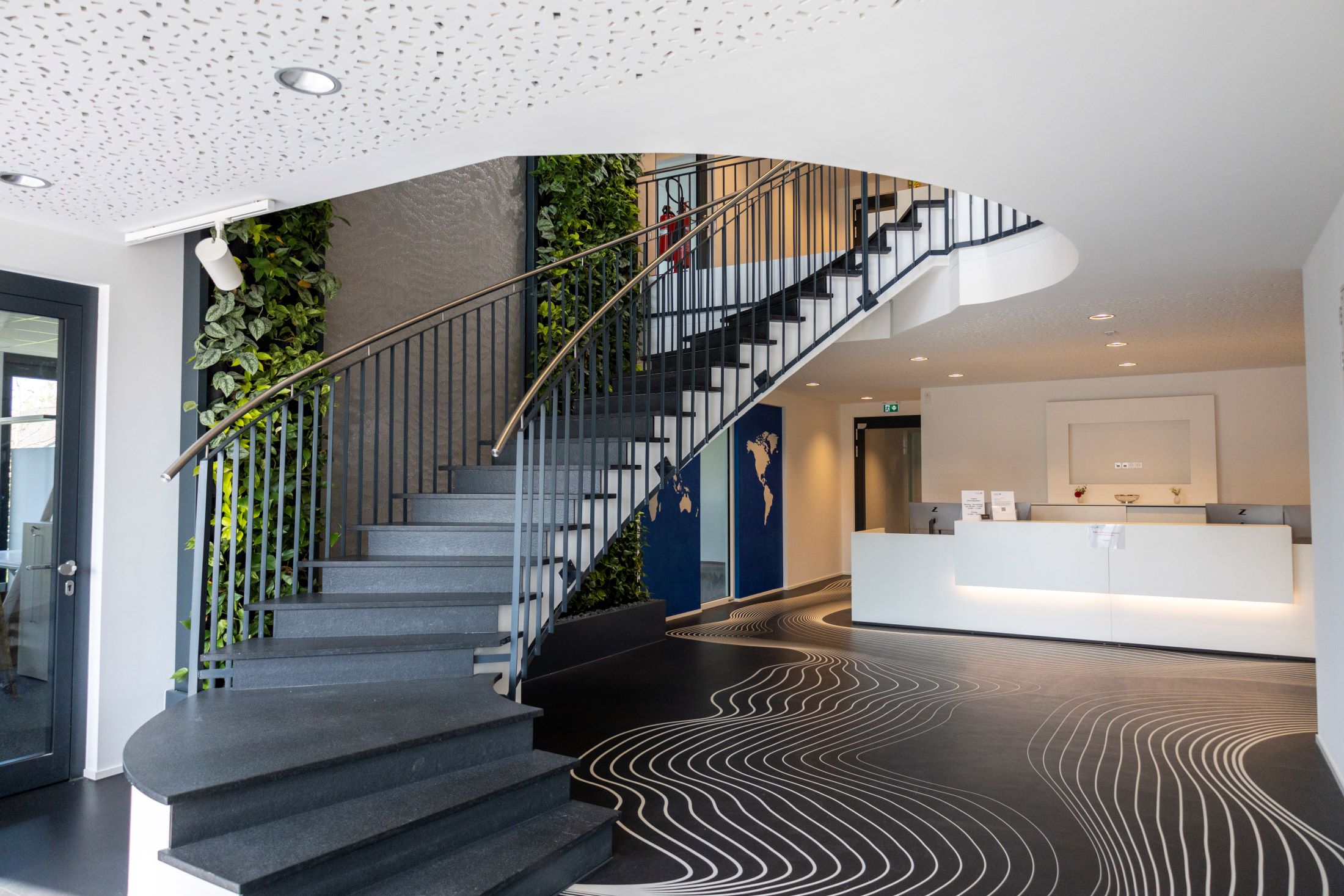 Lobby von Kohnle & Partner mit einer stilvollen Treppe, begrünten Wänden und einem professionellen Empfangsbereich, der Besucher willkommen heißt.
