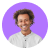 Smiling person with curly hair wearing a white shirt and white earbuds on a white background.