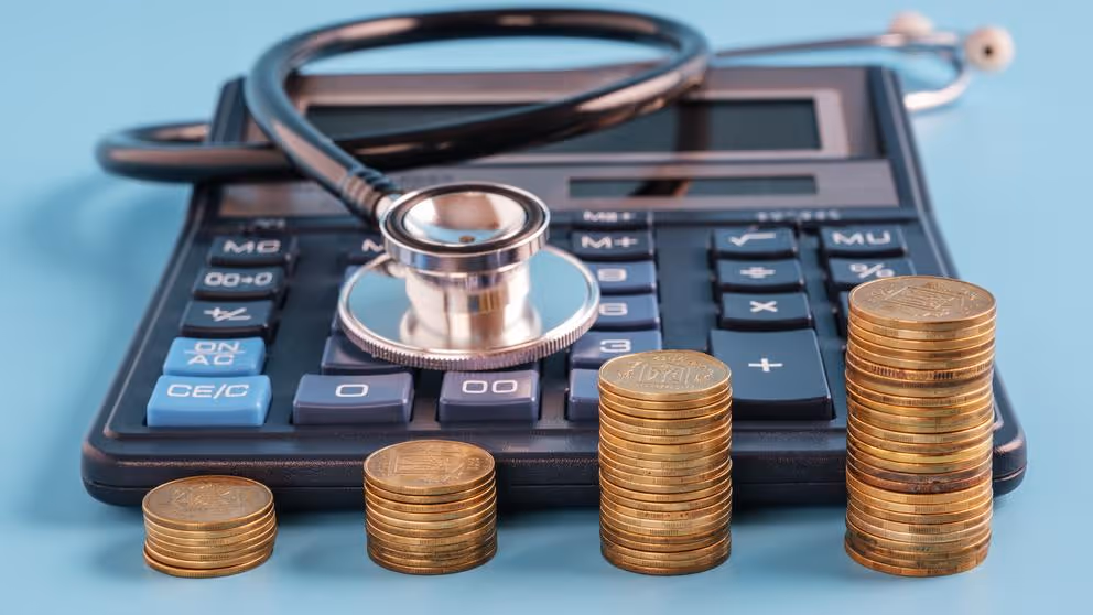 Four stacks of coins in ascending order next to a calculator and stethoscope.