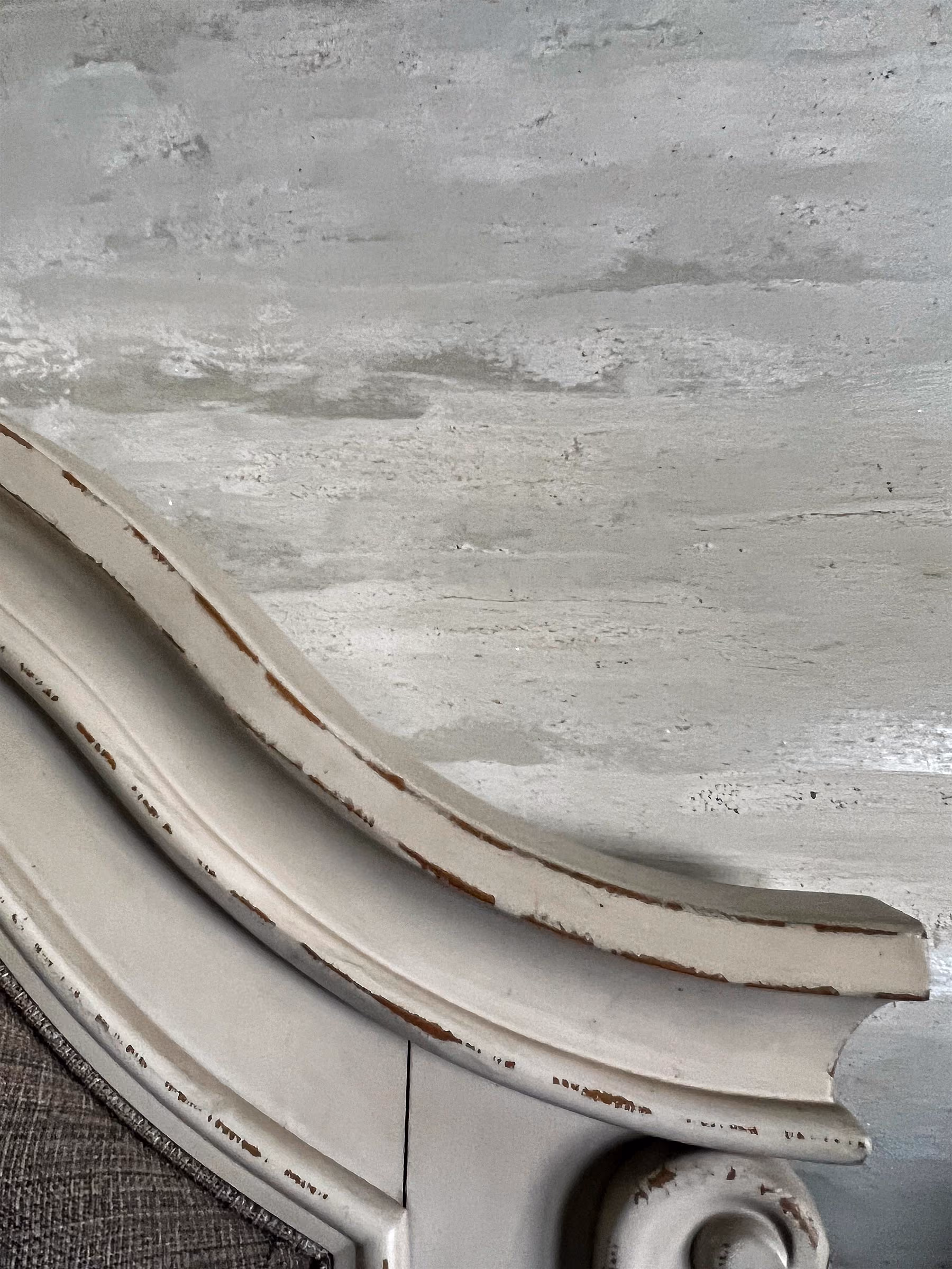 A close-up view of a decorative wooden trim, featuring elegant curves and distressed paint, set against a softly textured, light-colored wall.