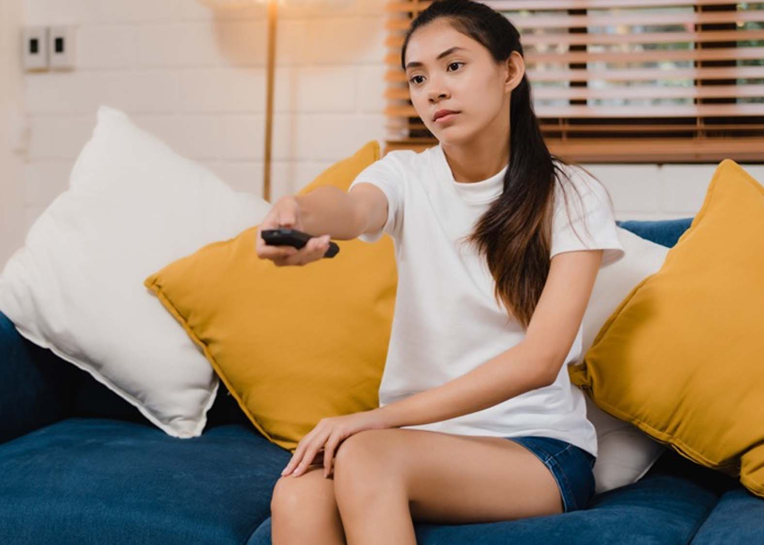 Girl pointing remote at TV, while watching FAST channels on big screen