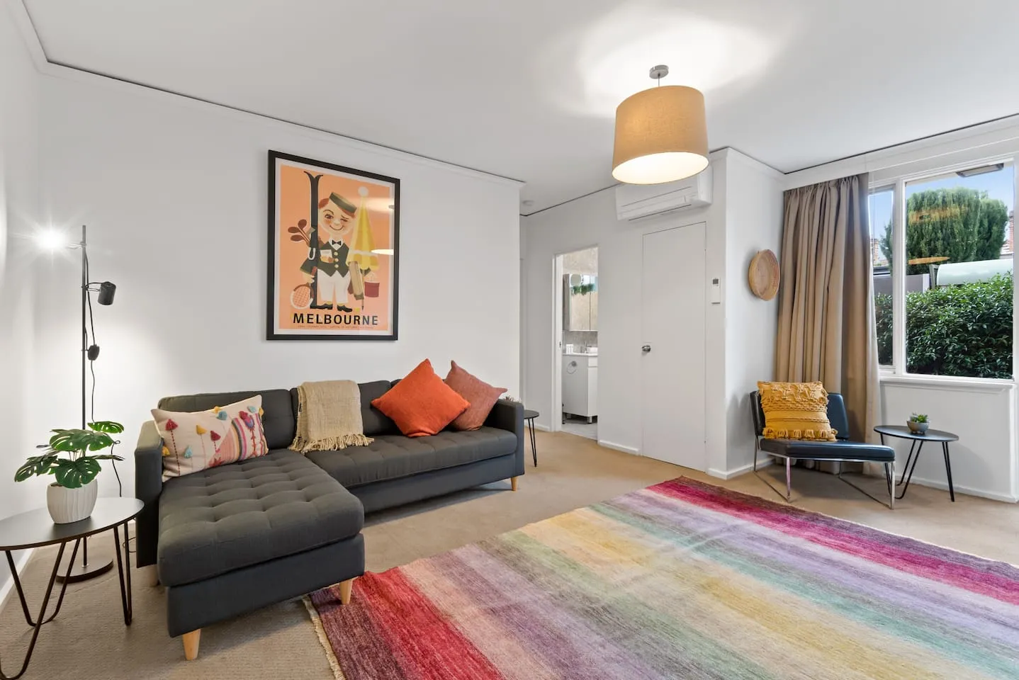 The living room is a fun and vibrant space with retro look wall art, a rainbow rug and bright throw pillows on the cosy chaise lounge.
