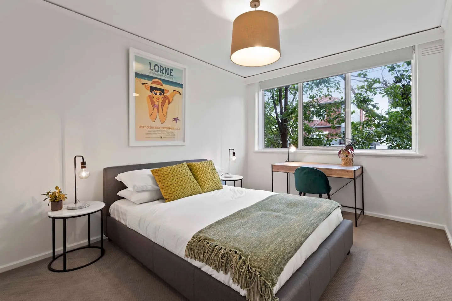The primary bedroom features a beautifully styled queen-sized bed with an upholstered frame, soft throw pillows, and a blanket between marble-look side tables.