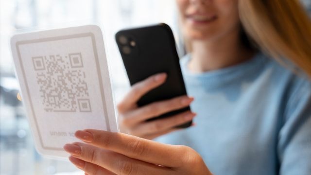 Mulher de cabelos claros utilizando celular para escanear QR code em placa segurada com a mão