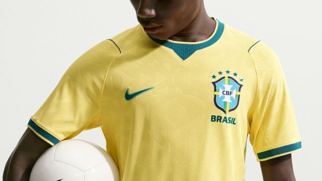 Homem de pele negra com a camiseta amarela da seleção brasileira segurando uma bola de futebol branca.