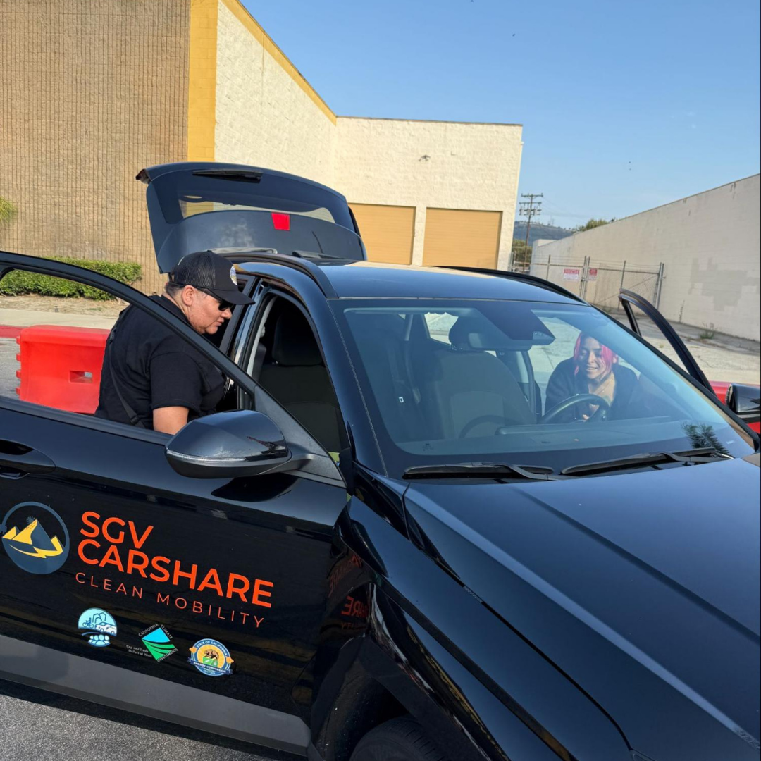 A person stands next to a black SGV CarShare electric vehicle.