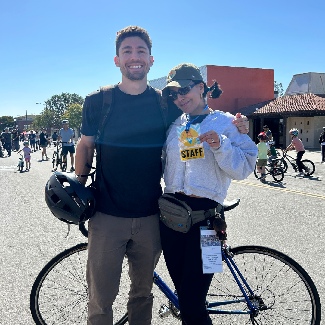 Carly poses with a fellow cyclist at an open streets event, holding her staff badge and smiling.