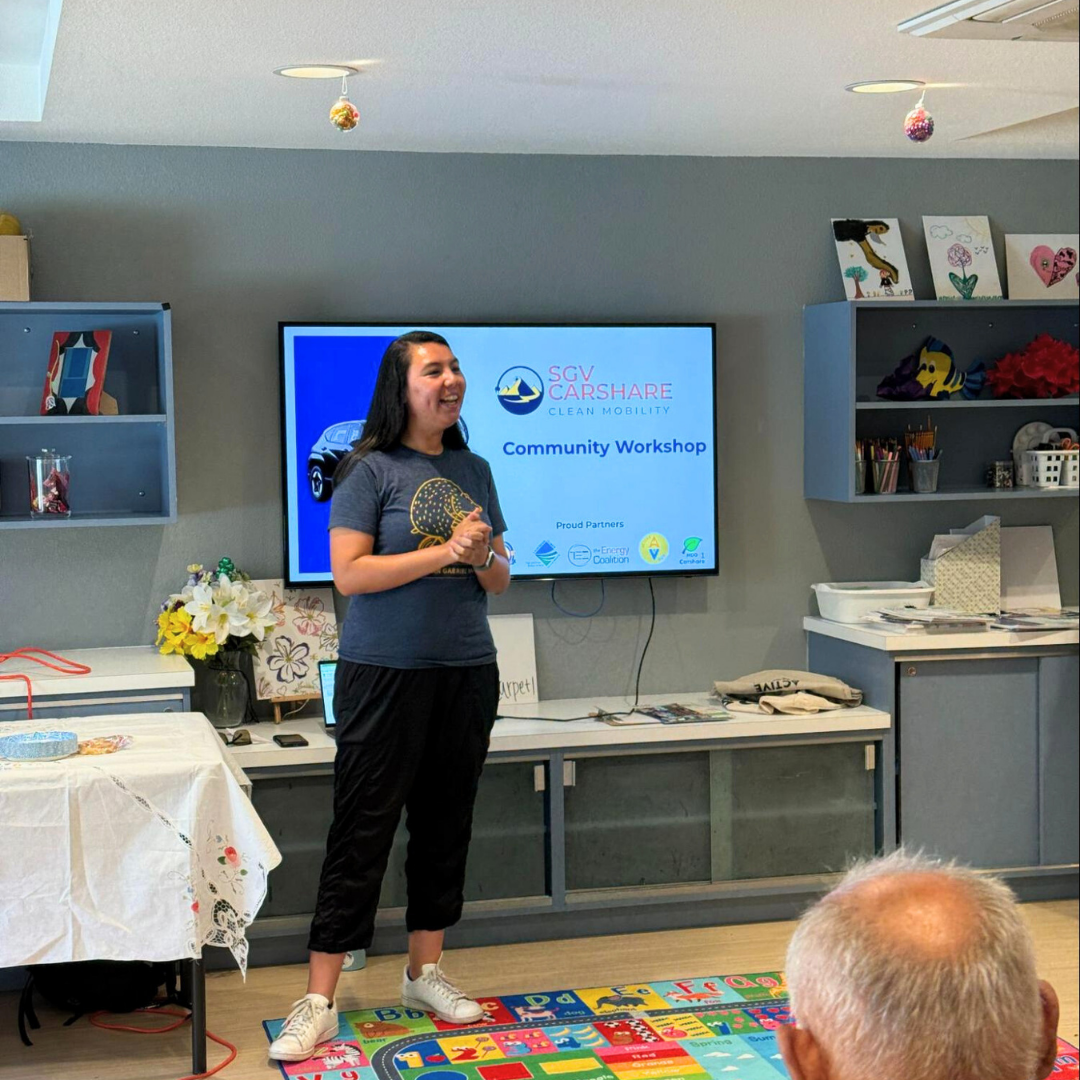 A woman speaks at a community workshop in front of a screen displaying “SGV Carshare Clean Mobility.