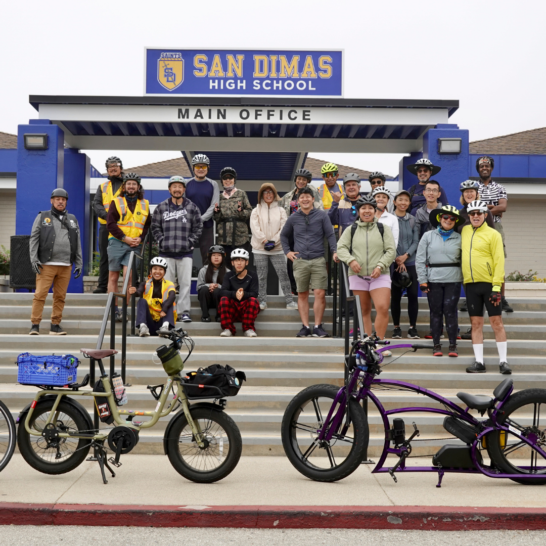 A large group of cyclists poses on the steps of San Dimas High School before a community ride.