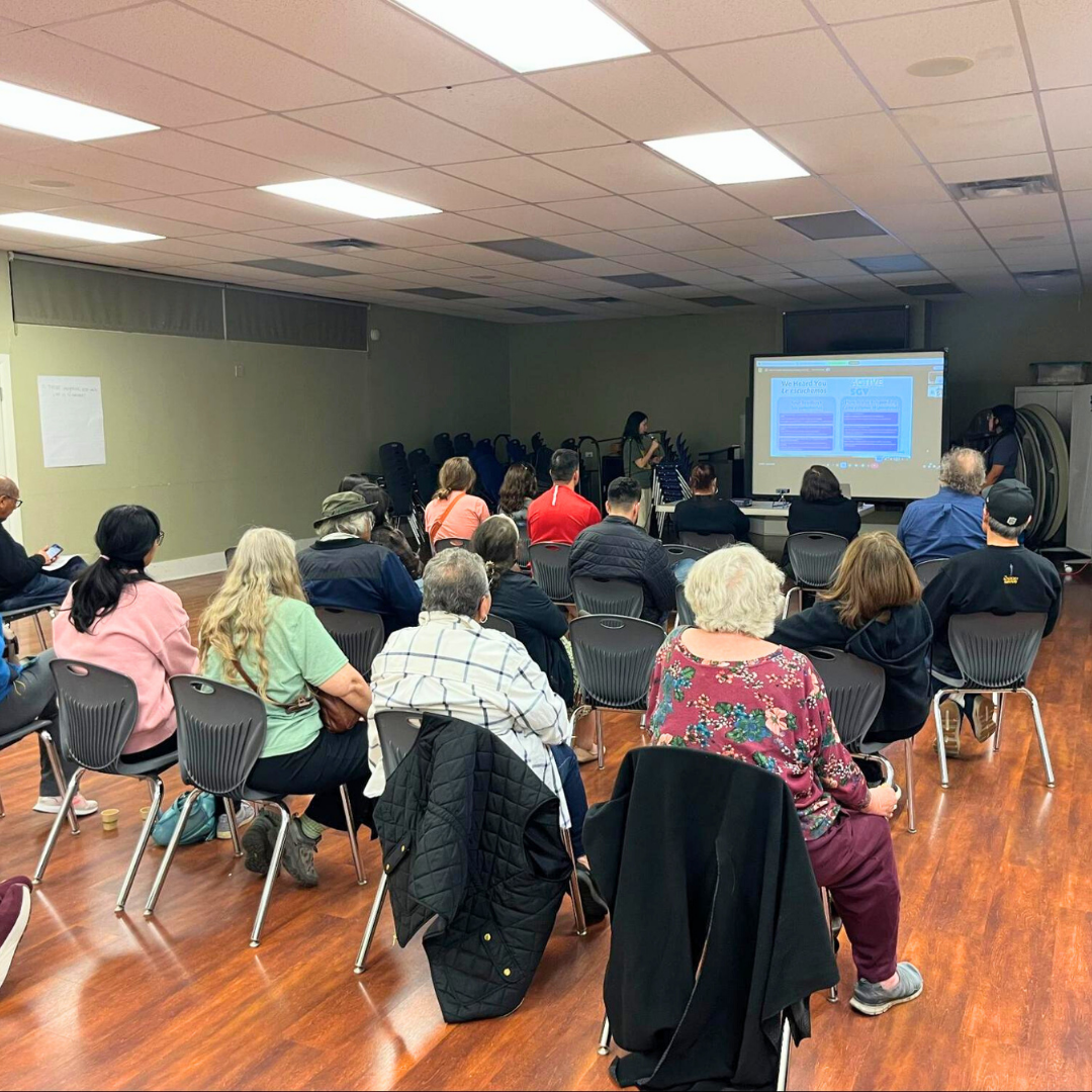 Residents sit in chairs facing a presentation screen during a community meeting.