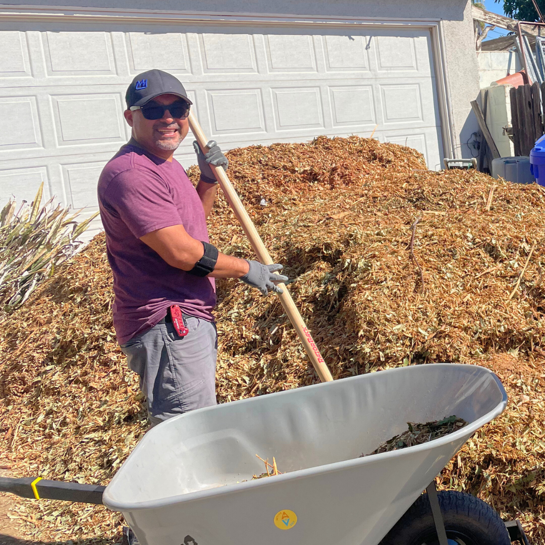 A volunteer smiles while spreading mulch with a shovel during a sheet mulching workday.