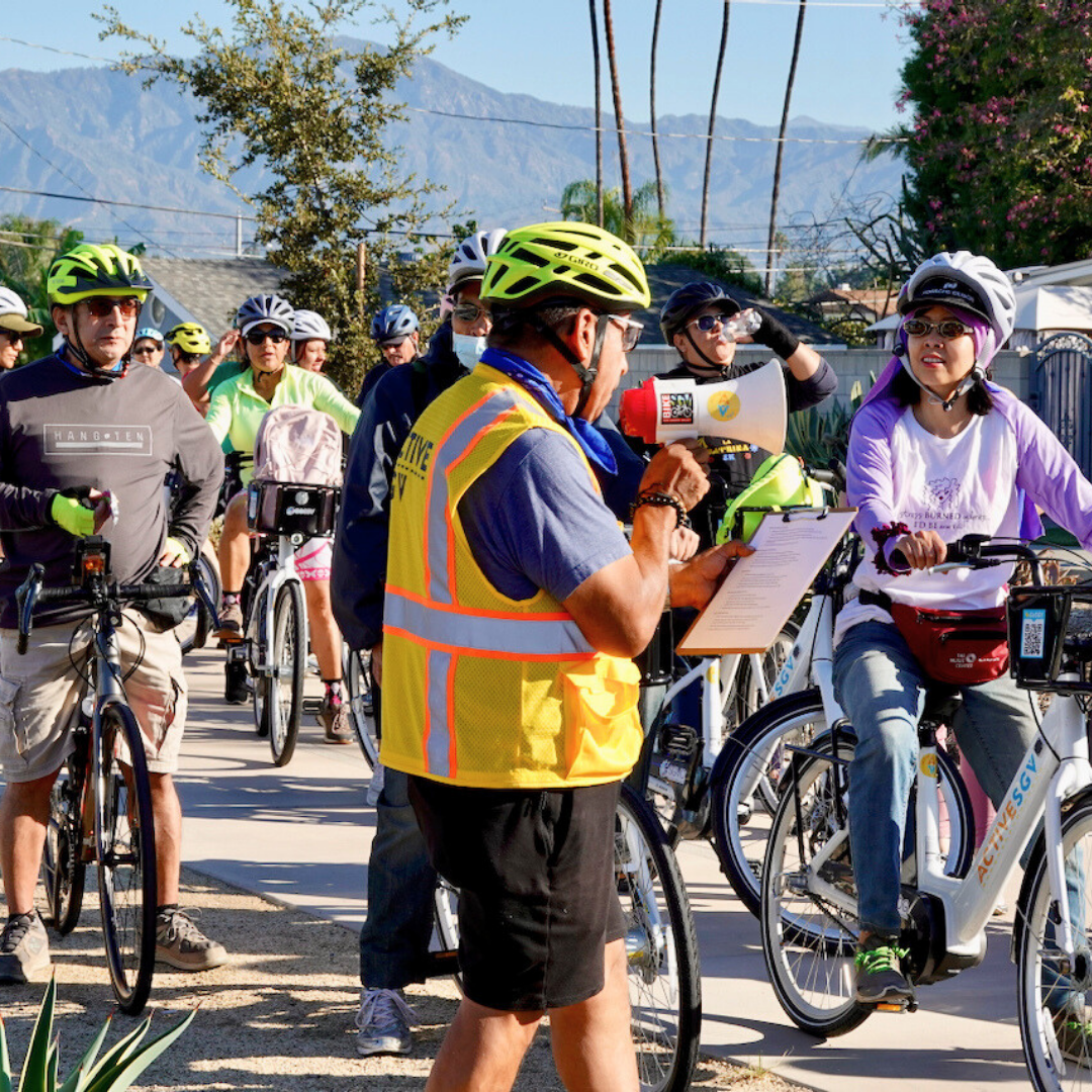 A group of cyclists lines up at the start of an Easy Access group ride, with mountains in the background.