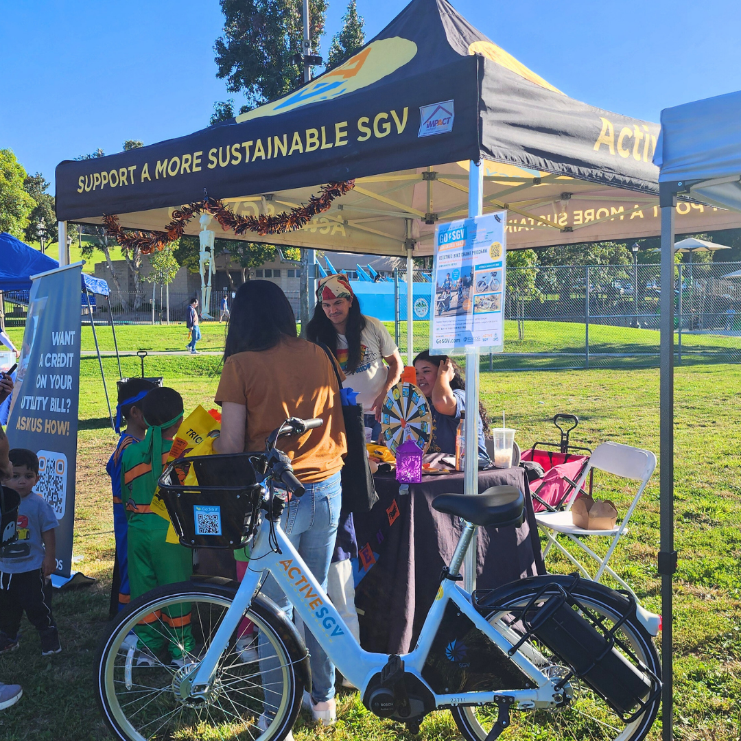 Community members stop by the ActiveSGV and GoSGV booth decorated for Halloween in a park.