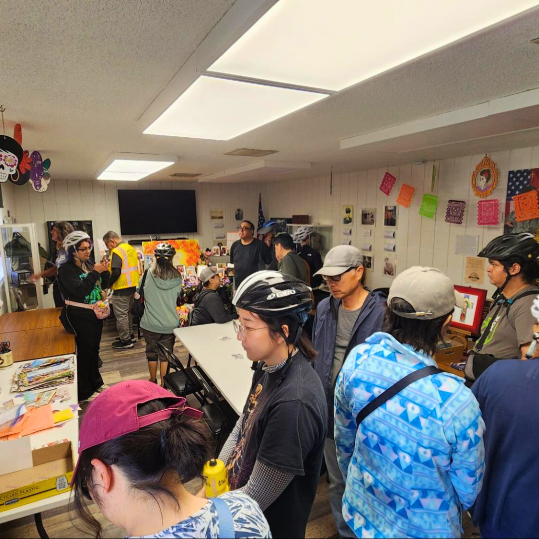 A crowd of people wearing helmets stand inside a community room with tables, decorations, and activity supplies.