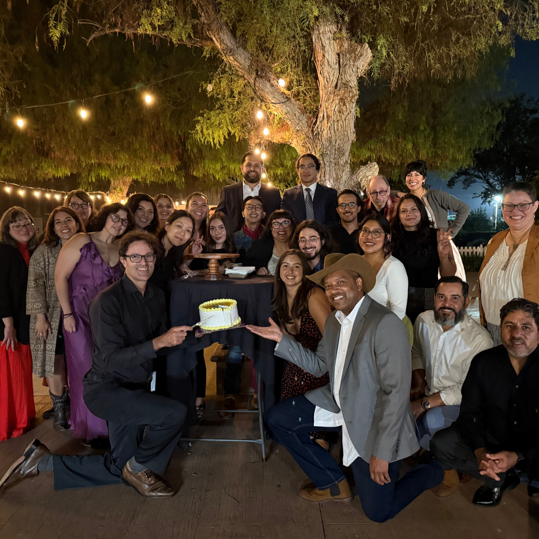 A large group of people pose together outdoors under string lights at a nighttime gathering.