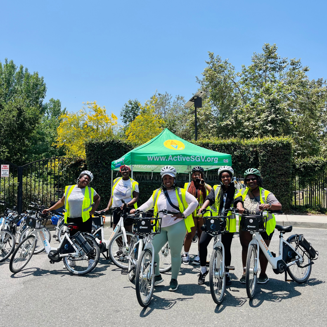 A group of riders pose with E-bikes in front of an ActiveSGV tent.