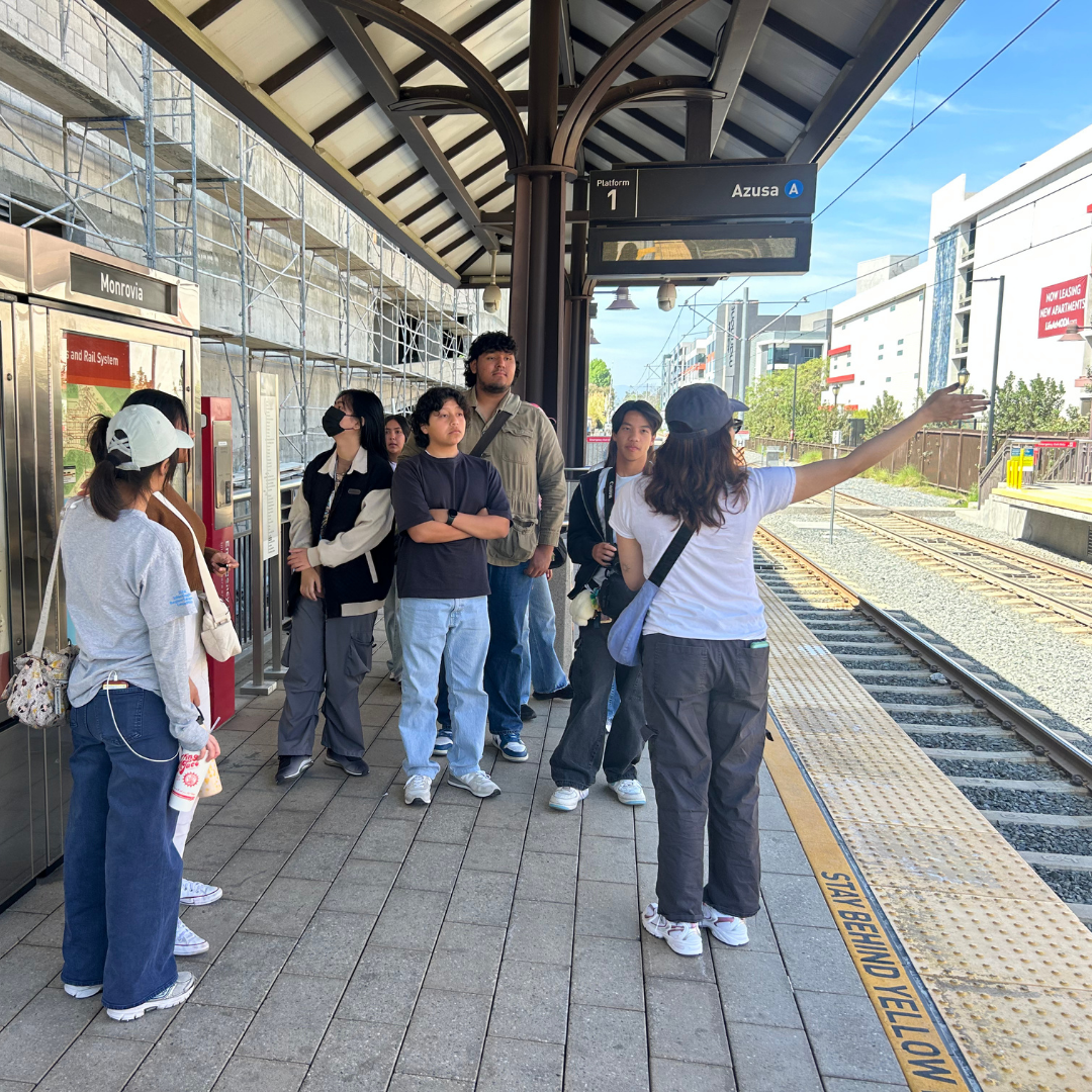 A group of youth stands on a Metro platform while a guide gestures toward the tracks.