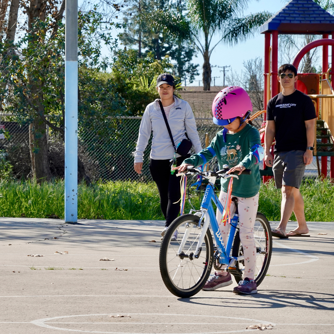 Child on a blue bicycle and wearing a pink helmet is learning to ride