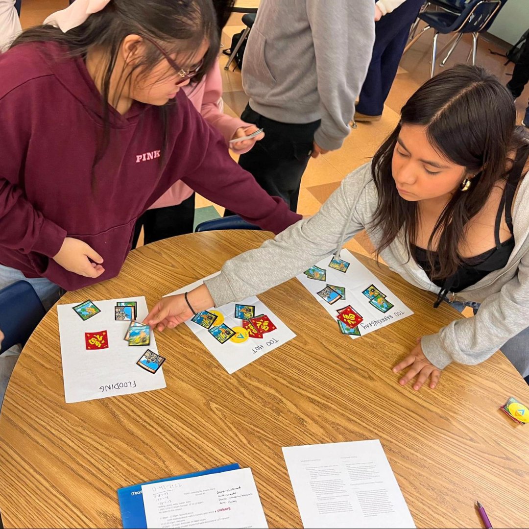 Two students arrange activity cards on labeled sheets at a table.