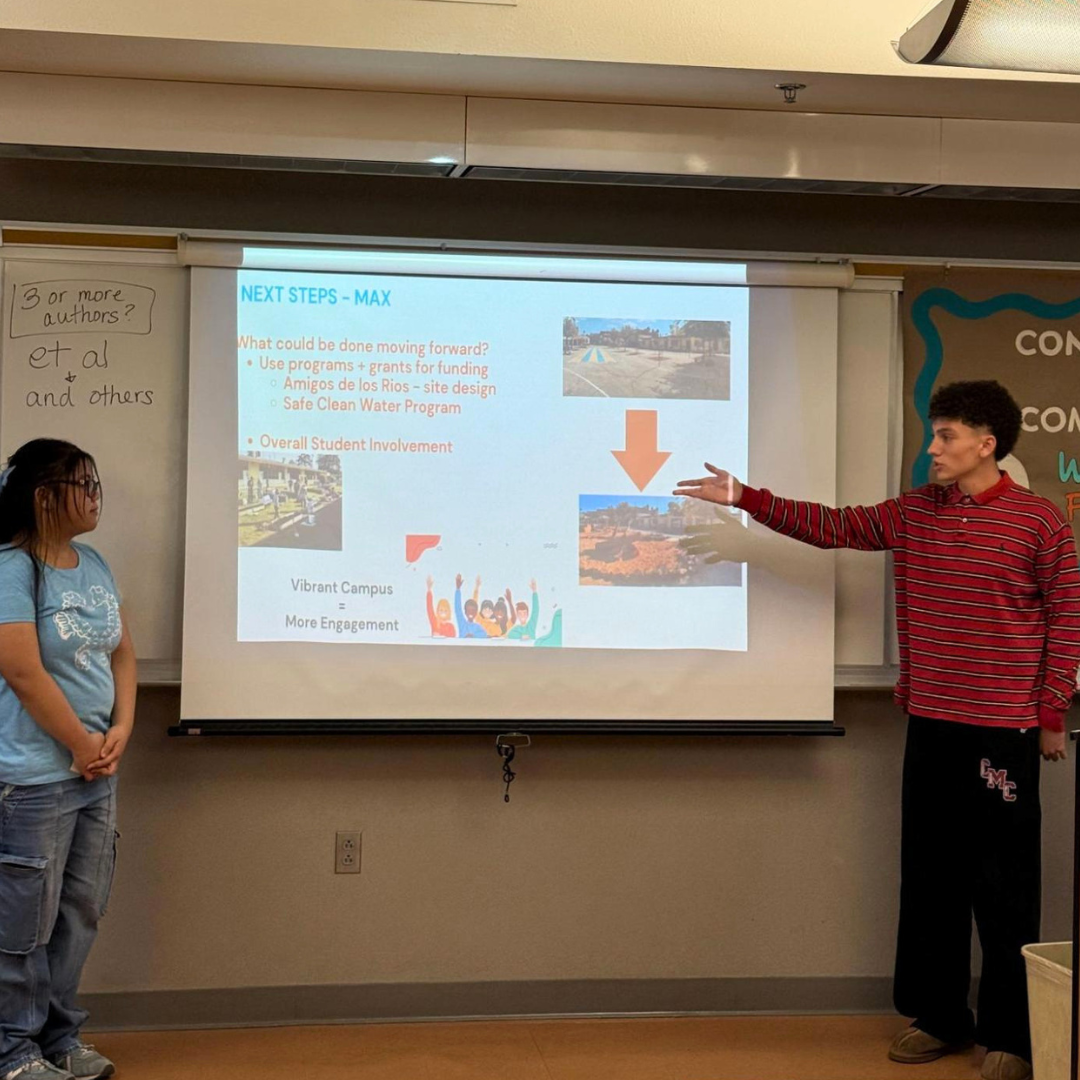 Two students stand in front of a projector screen during a classroom presentation.