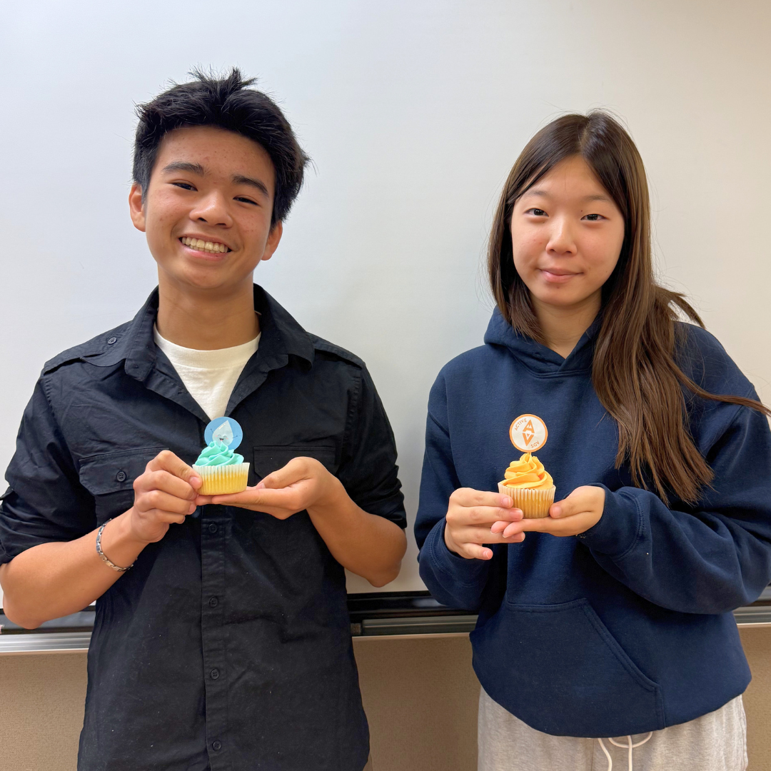 Two students hold decorated cupcakes and smile for the camera.